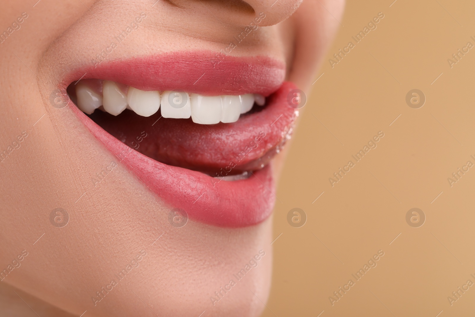 Photo of Young woman licking her teeth on beige background, closeup