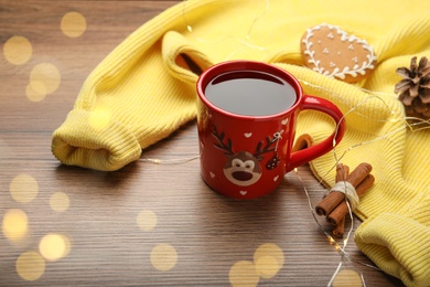 Cup of hot drink with yellow sweater and Christmas lights on wooden table