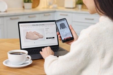 Woman with laptop and smartphone shopping online at wooden table in kitchen, closeup