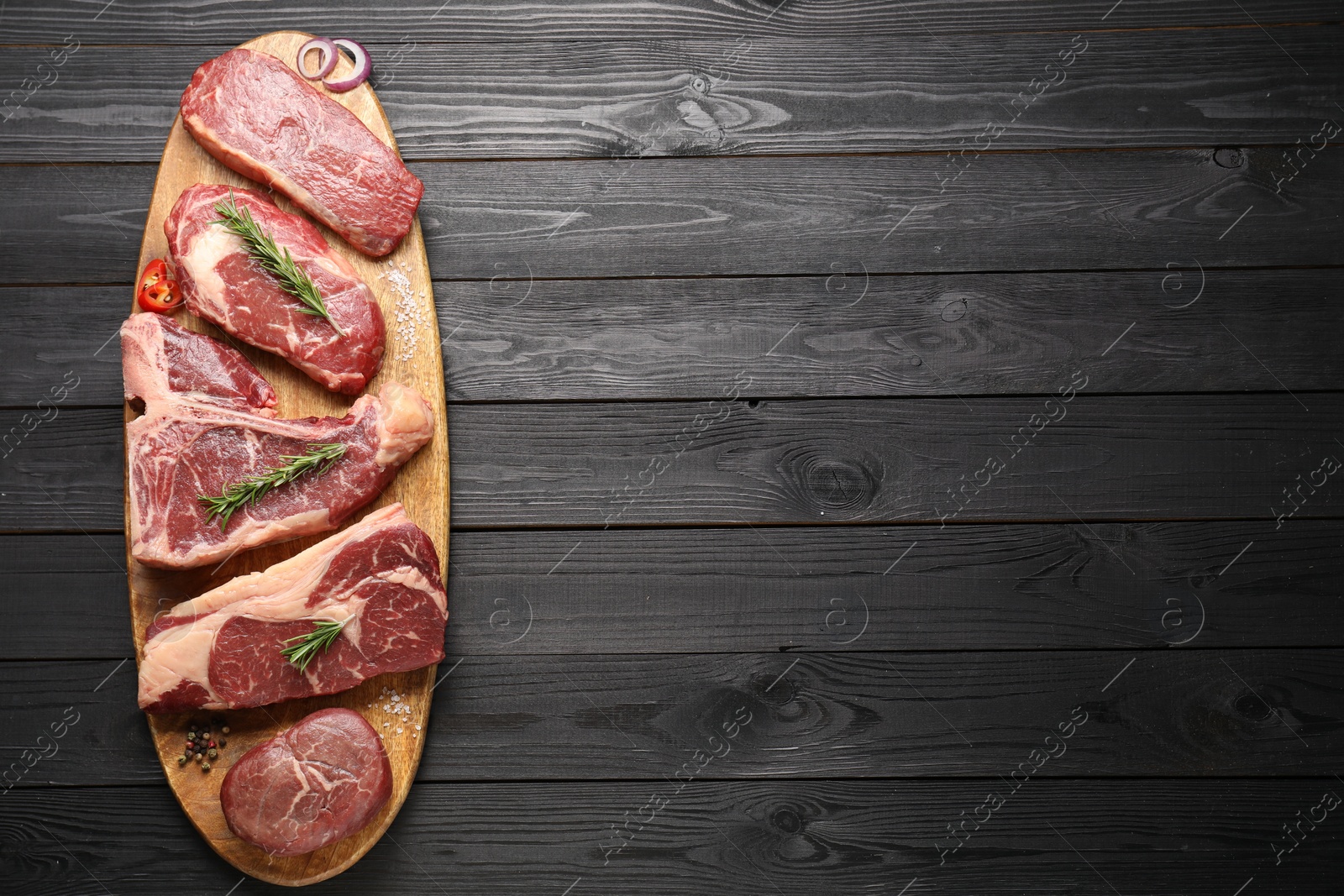 Photo of Pieces of raw beef meat and spices on black wooden table, top view. Space for text