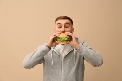 Young man eating tasty burger on color background