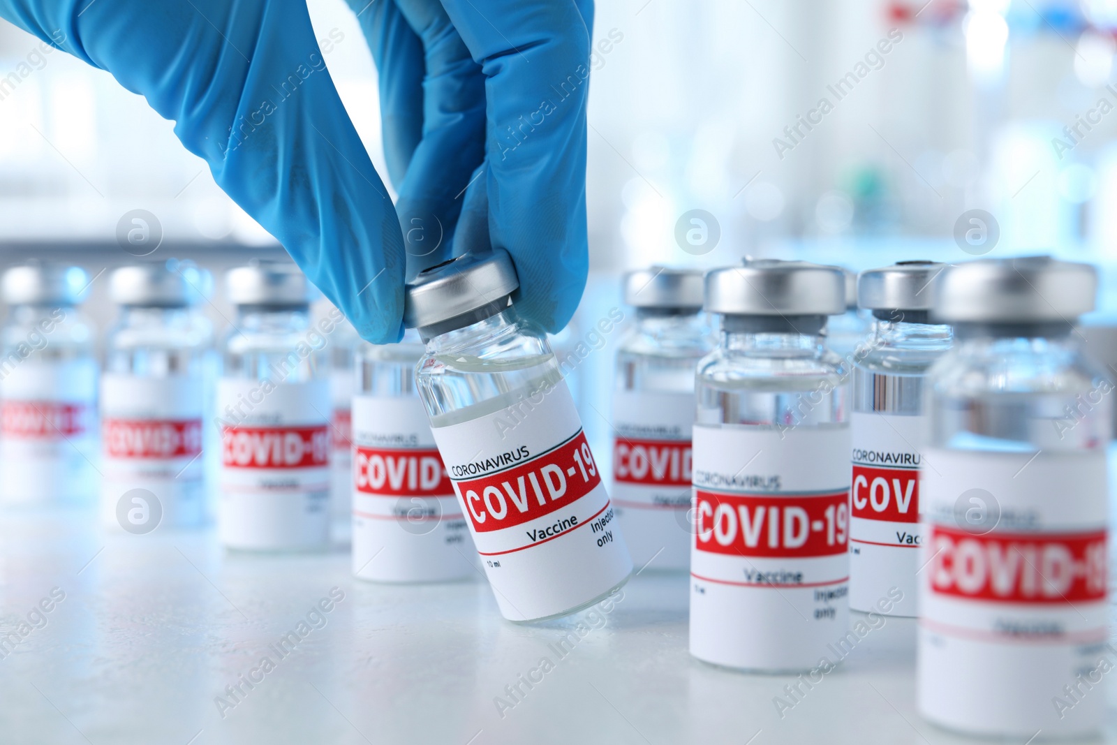 Photo of Doctor taking glass vial with COVID-19 vaccine from table, closeup