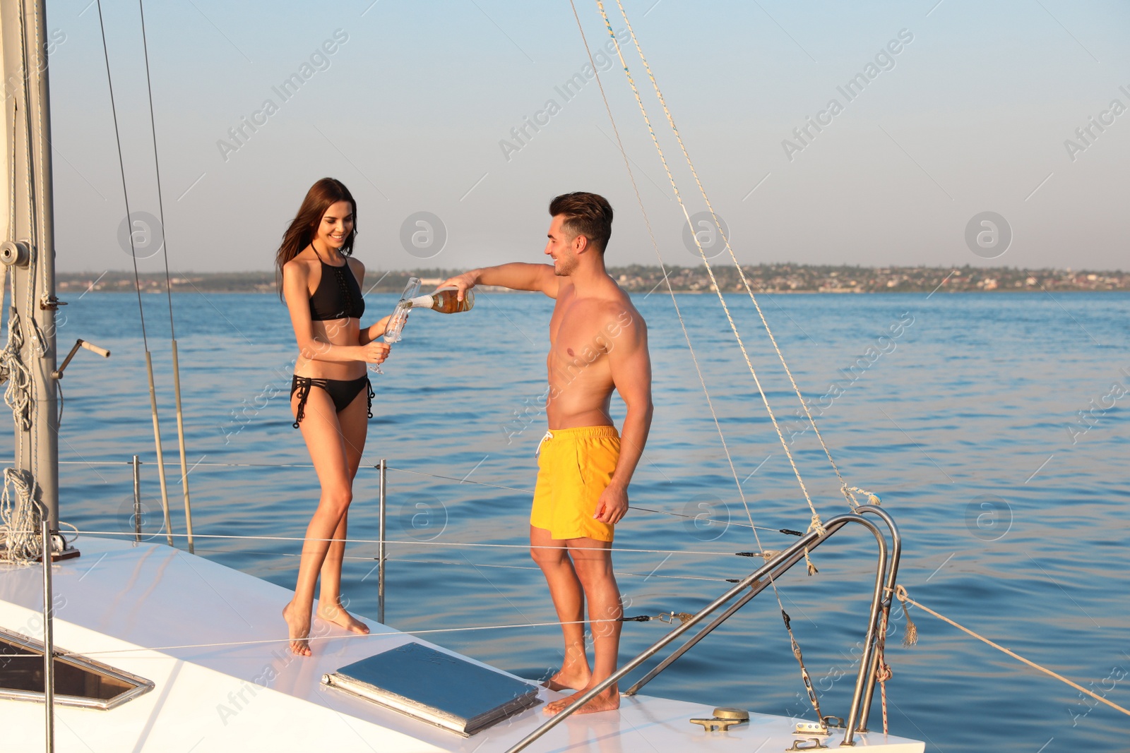 Photo of Young man and his girlfriend in bikini drinking champagne on yacht