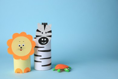 Photo of Toy lion, zebra made from toilet paper hubs and plasticine turtle on light blue background, space for text. Children's handmade ideas