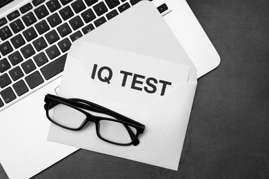 Paper with words IQ Test in envelope, glasses and laptop on black table, flat lay