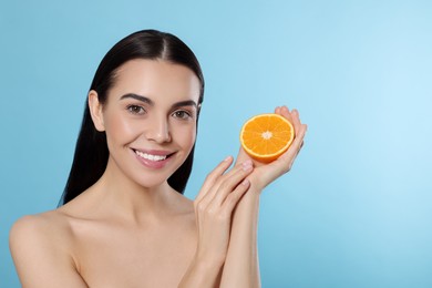 Woman holding half of orange on light blue background, space for text. Spa treatment