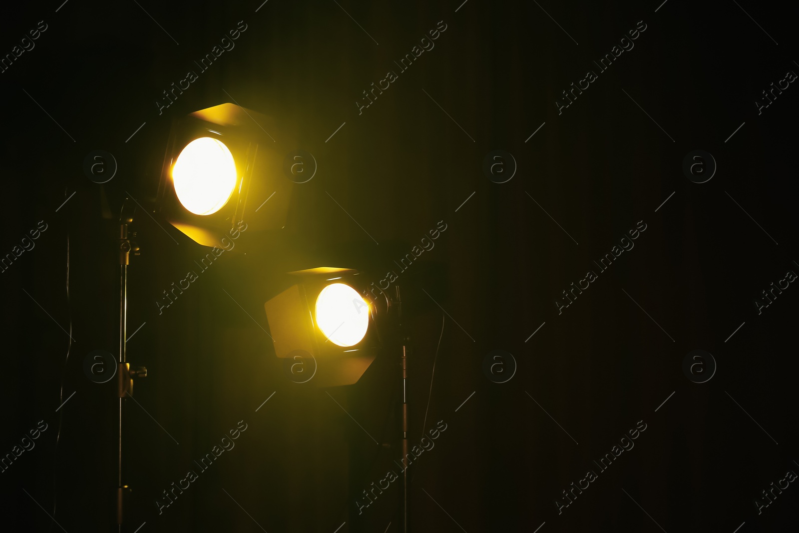 Photo of Bright yellow spotlights on dark stage, space for text