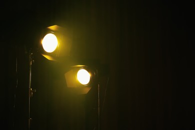 Photo of Bright yellow spotlights on dark stage, space for text