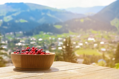 Photo of Bowl of fresh ripe berries on table against mountain landscape