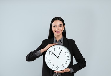 Photo of Businesswoman holding clock on light grey background. Time management