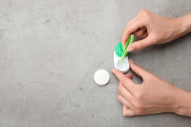 Photo of Woman taking contact lens from case with tweezers at grey table, top view. Space for text