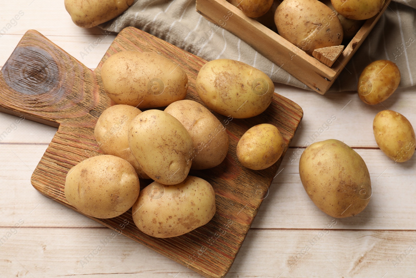 Photo of Raw fresh potatoes and cutting board on light wooden table, top view