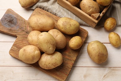 Raw fresh potatoes and cutting board on light wooden table, top view