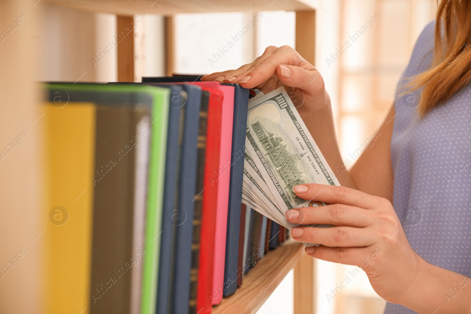 Photo of Woman hiding money between books on shelf indoors, closeup. Financial savings