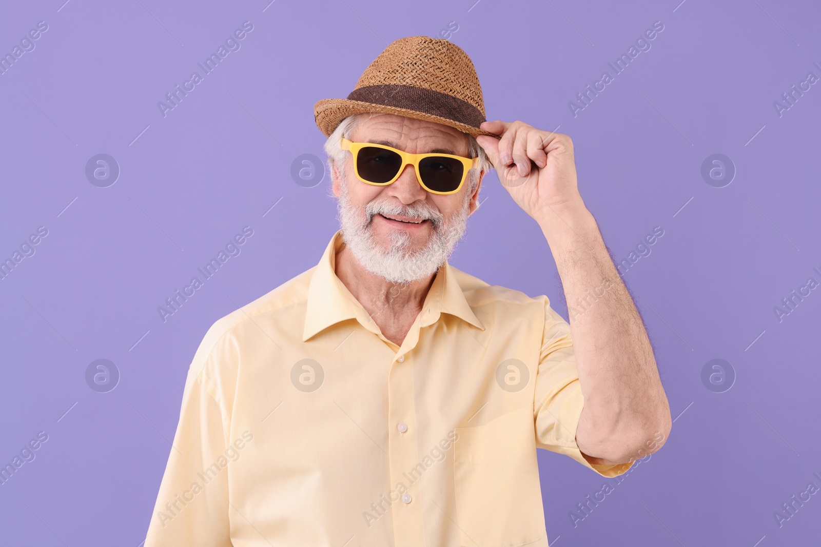 Photo of Portrait of stylish grandpa with sunglasses and hat on purple background