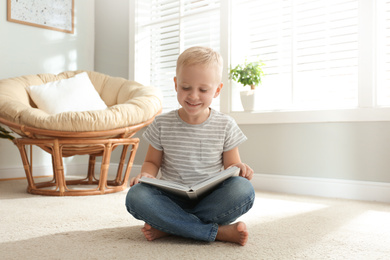 Cute little boy reading book on floor at home