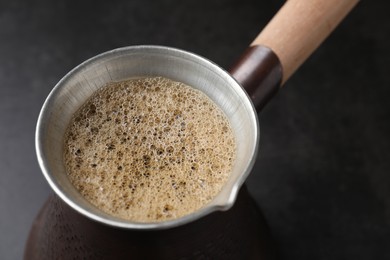 Photo of Turkish coffee in cezve on dark table, closeup