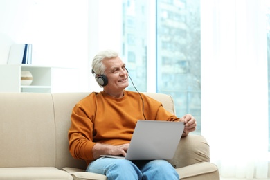 Photo of Portrait of mature man with laptop and headphones on sofa indoors