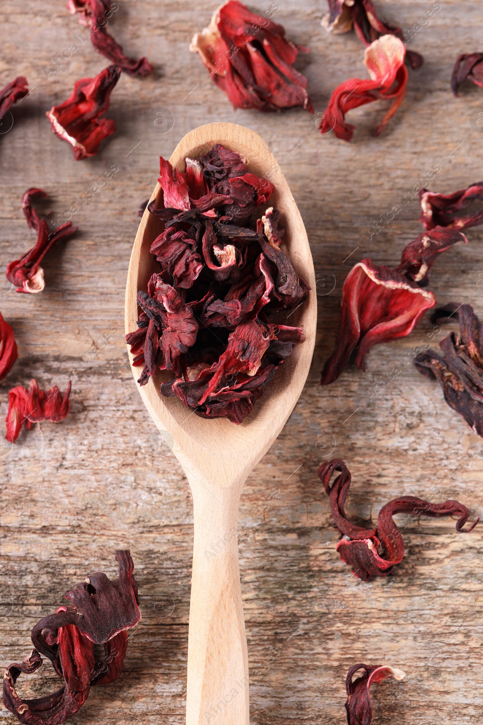 Photo of Spoon with dry hibiscus tea on wooden table, flat lay