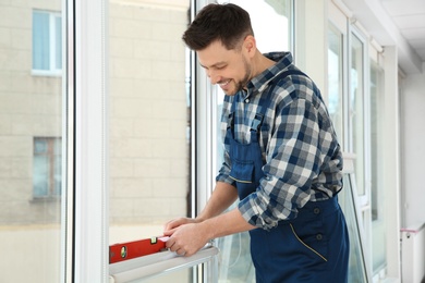 Photo of Construction worker using bubble level while installing window indoors