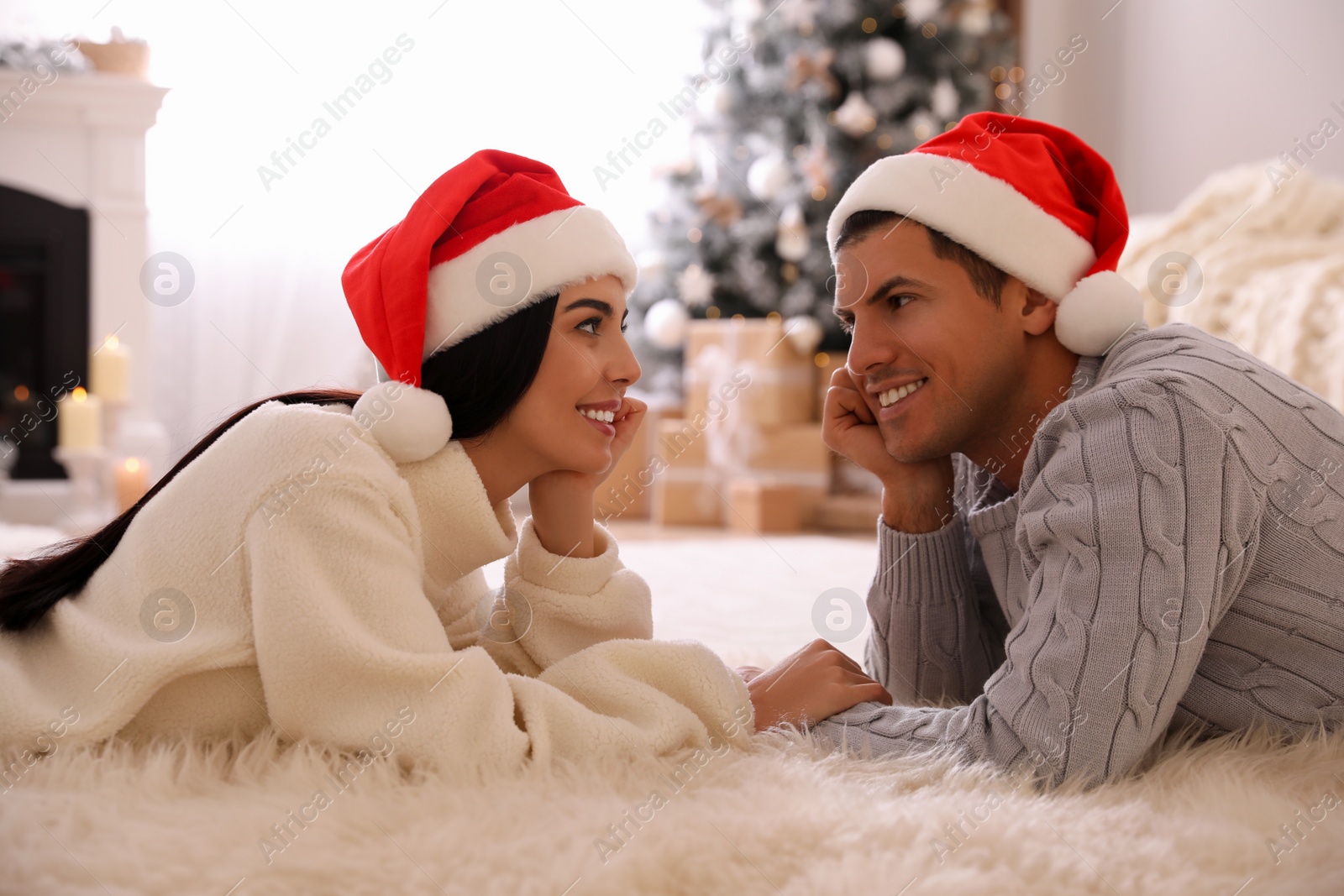 Photo of Couple lying on faux fur in room with Christmas tree and gift boxes