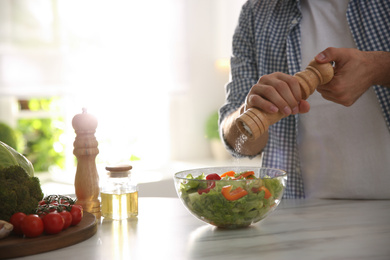 Photo of Man cooking salad at table in kitchen, closeup