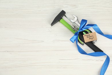 Photo of Happy Father's Day. Greeting card and set of tools tied with ribbon on light wooden table, top view. Space for text
