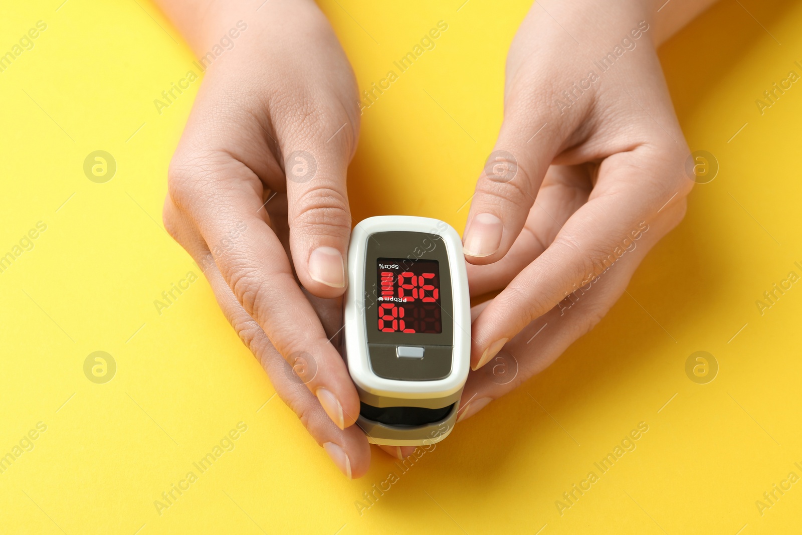 Photo of Woman holding fingertip pulse oximeter on yellow background, closeup