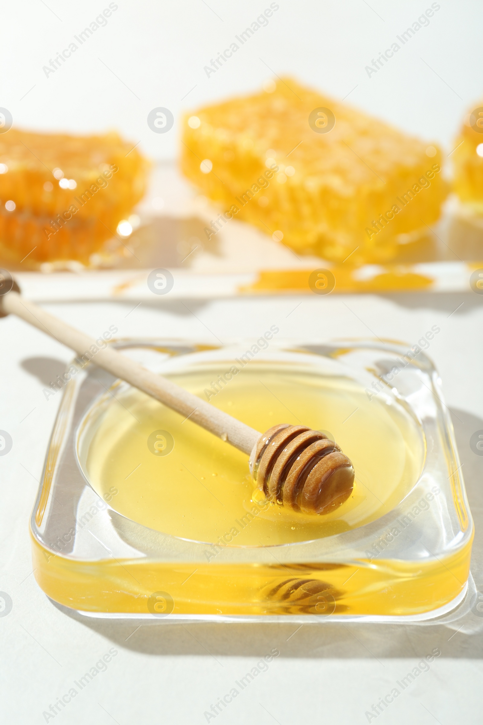 Photo of Bowl with tasty honey, natural honeycombs and dipper on white table