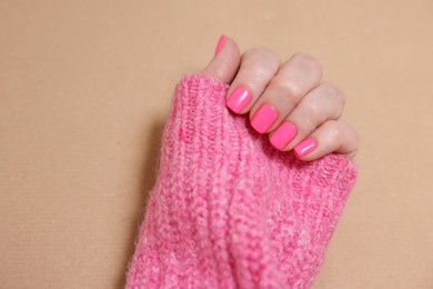 Woman showing her manicured hand with pink nail polish on dark beige background, closeup