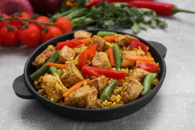 Photo of Serving pan of delicious rice with chicken and vegetables on light grey table, closeup
