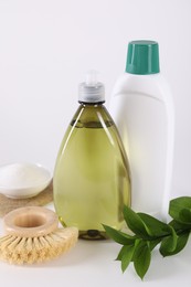 Bottles of cleaning product, brush, baking soda and green leaves on white background