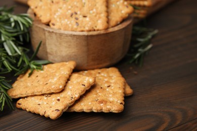 Photo of Cereal crackers with flax, sesame seeds and rosemary on wooden table, closeup. Space for text