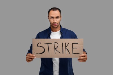 Man holding cardboard banner with word Strike on grey background