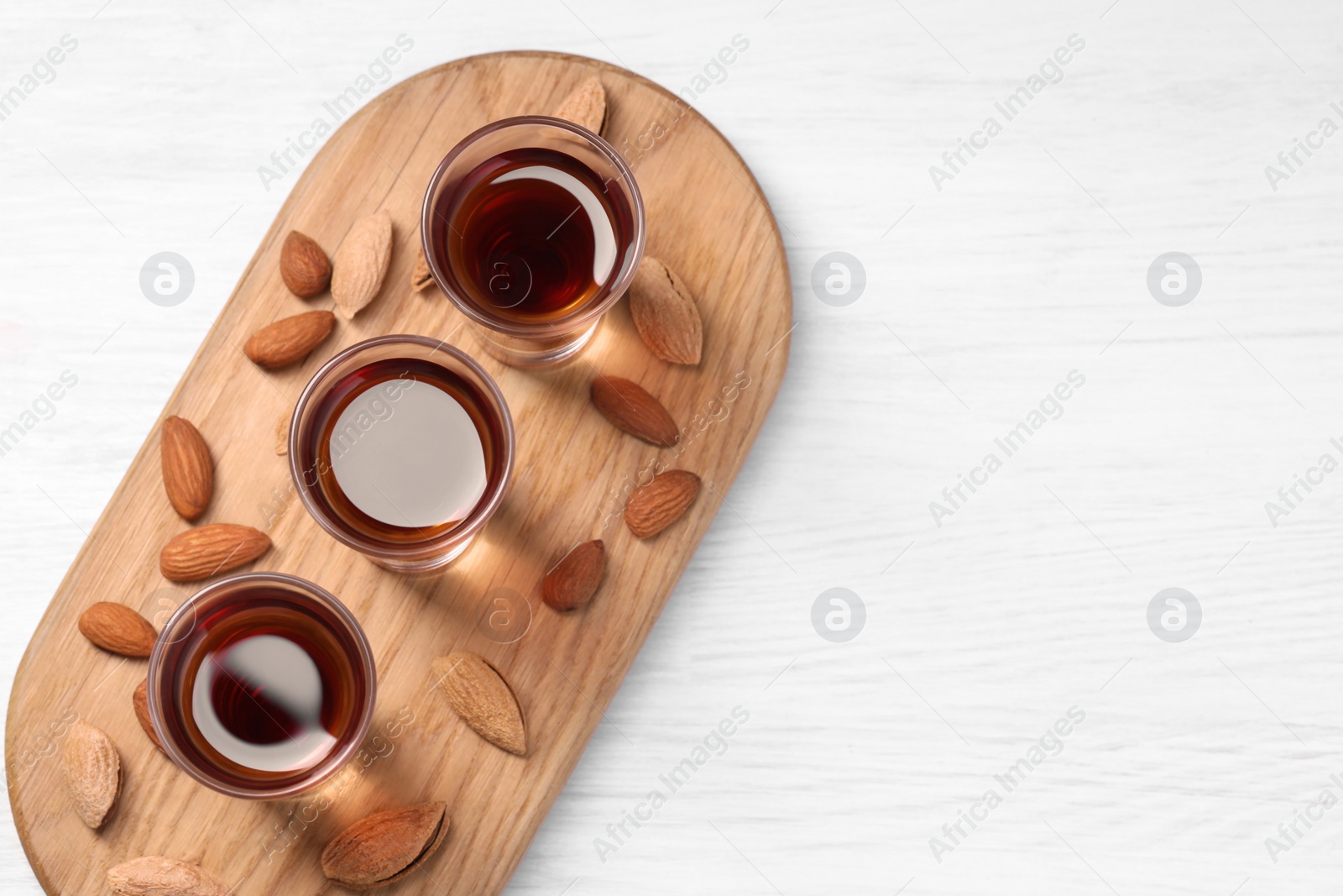 Photo of Shot glasses with tasty amaretto liqueur and almonds on white wooden table, top view. Space for text