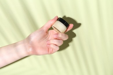 Woman holding jar of cream on green background, closeup. Space for text