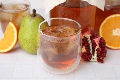 Photo of Tasty kombucha with ice cubes and fresh fruits on white tiled table, closeup