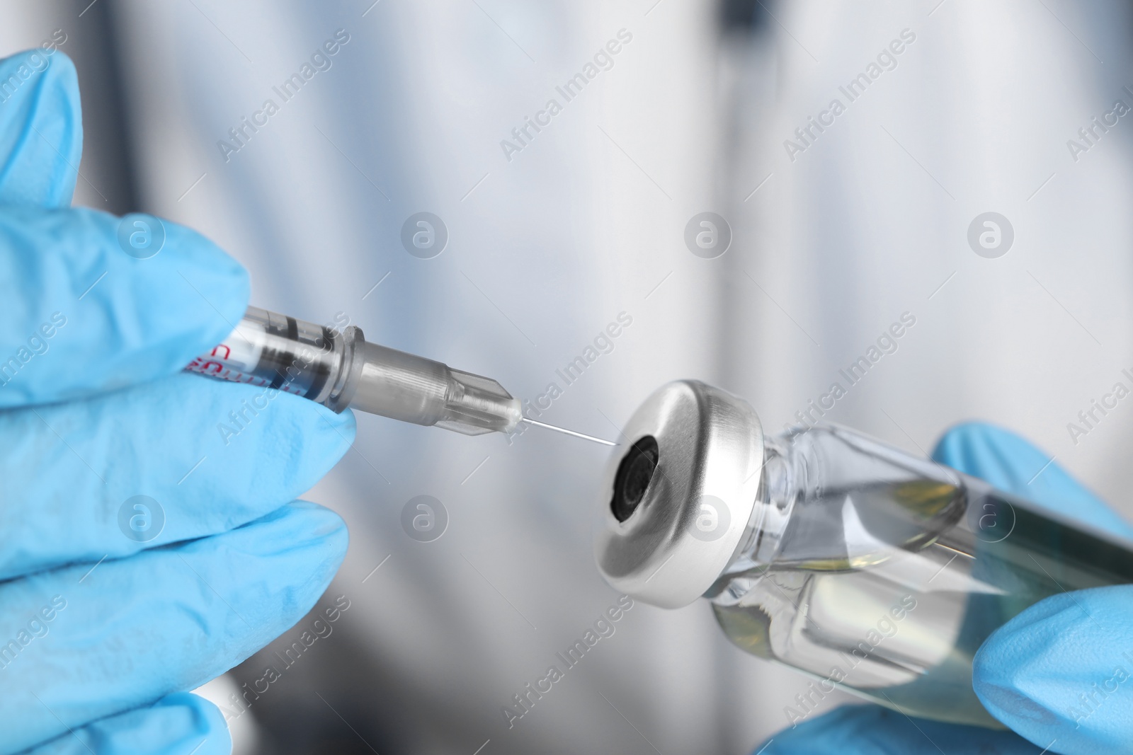 Photo of Doctor inserting syringe into glass vial with medication, closeup