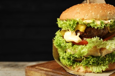 Photo of Burger with delicious patty on wooden table against dark background, closeup. Space for text