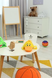 Photo of Different toys on white table and chairs in playroom. Kindergarten interior design