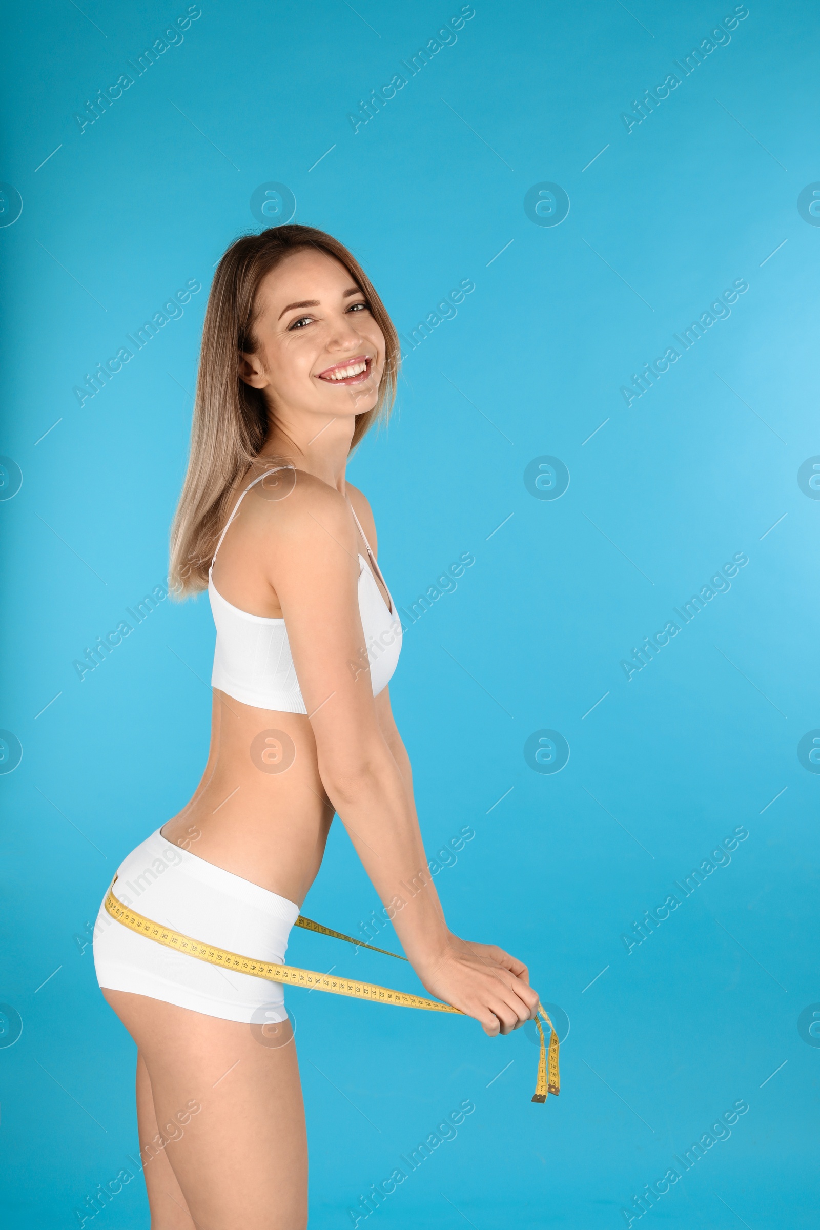 Photo of Slim woman measuring her hips on color background, space for text. Perfect body