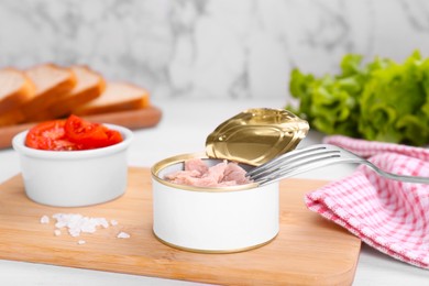 Photo of Tin can with canned tuna and fork on white table