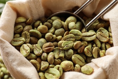 Photo of Green coffee beans and scoop in sackcloth bag, closeup