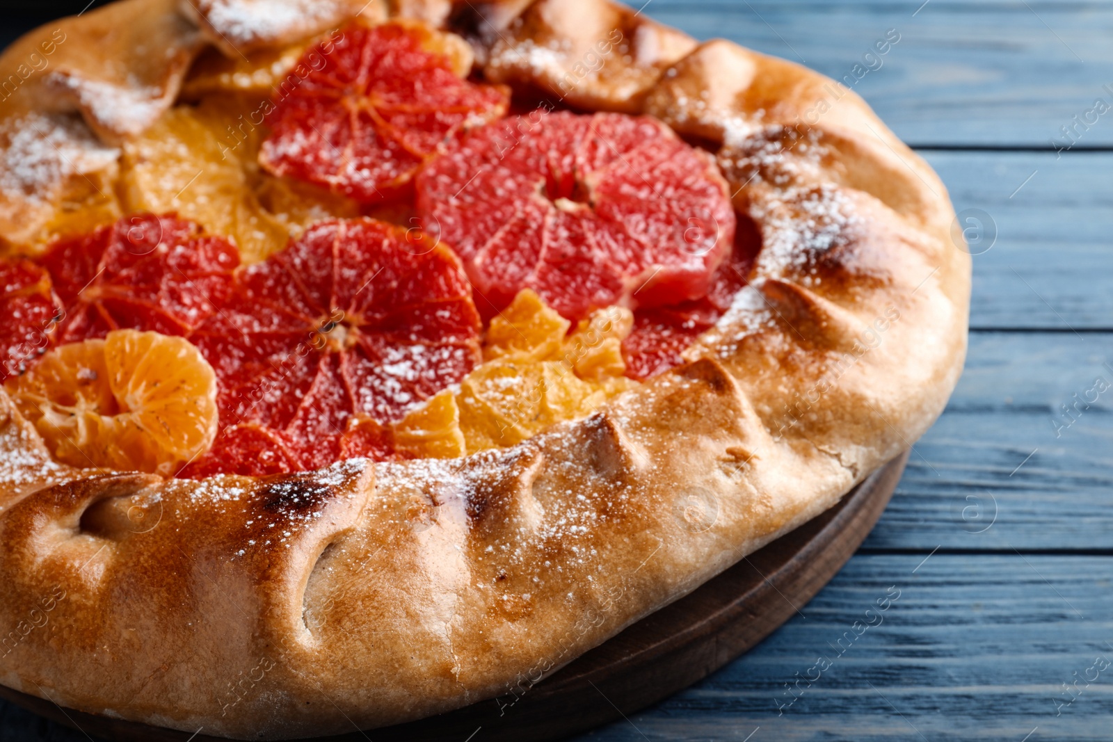 Photo of Delicious galette with citrus fruits on blue wooden table, closeup