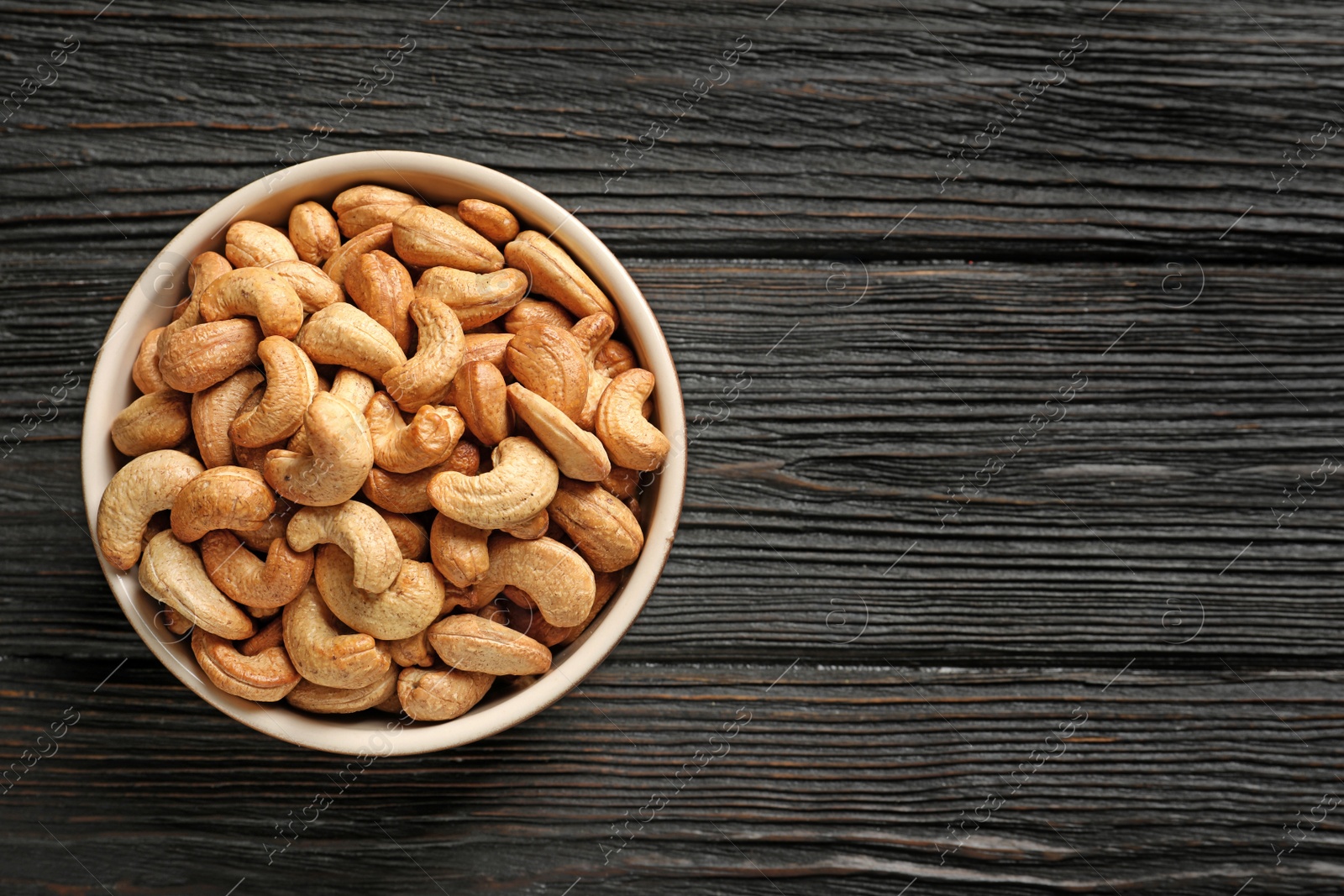 Photo of Bowl with cashew nuts on wooden table, top view. Space for text