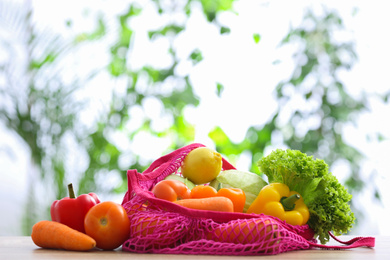 Net bag with vegetables on table against blurred background