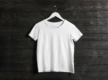 Photo of Hanger with white t-shirt on wooden background. Mockup for design