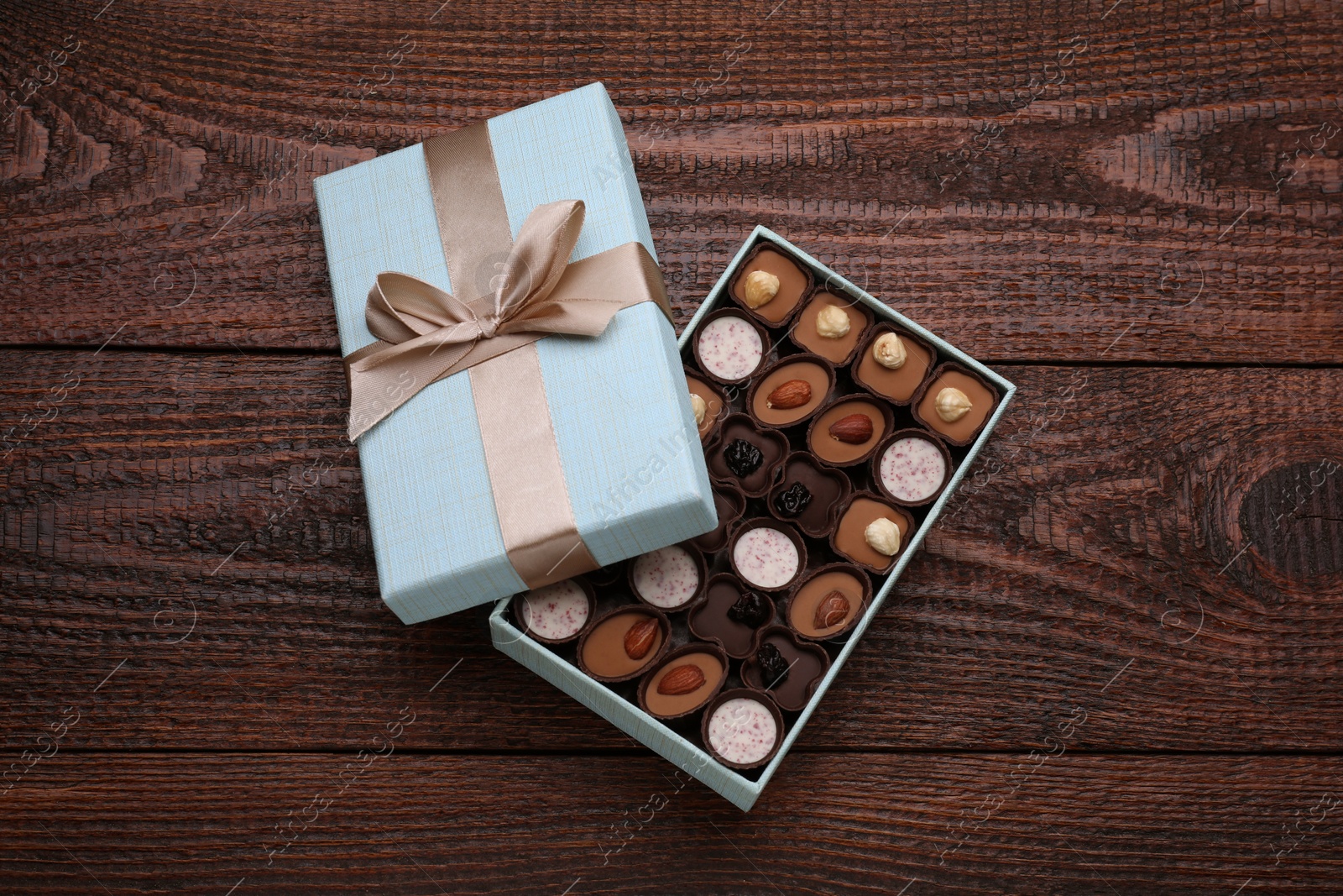 Photo of Open box of delicious chocolate candies on wooden table, top view