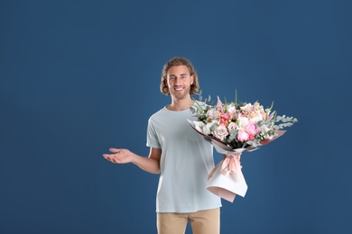 Photo of Young handsome man with beautiful flower bouquet on blue background