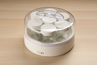 Modern yogurt maker with empty jars on wooden table